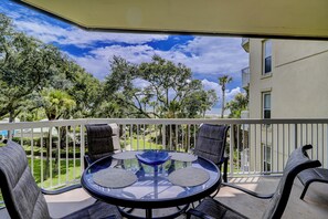 Un balcon doté d’une table ronde en verre et de quatre chaises, offrant une vue sur un jardin bien entretenu et sur un bâtiment situé au loin.