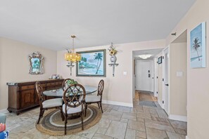 A dining area with a round table and chairs, a wooden cabinet, and wall-mounted decorations including a painting and a vase. - 11th Floor Corner Unit - Views Galore! (Pensacola Beach)