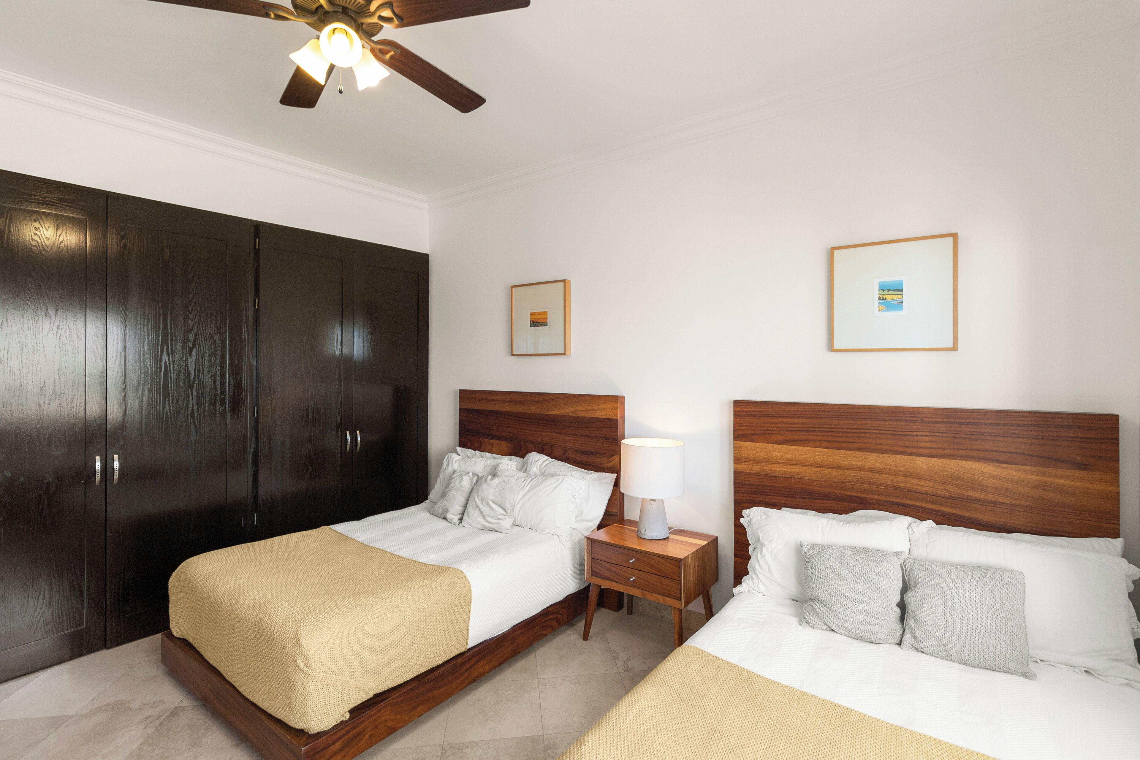 Une chambre d’hôtel avec deux lits, une armoire, une table de chevet avec une lampe et des ventilateurs de plafond.
