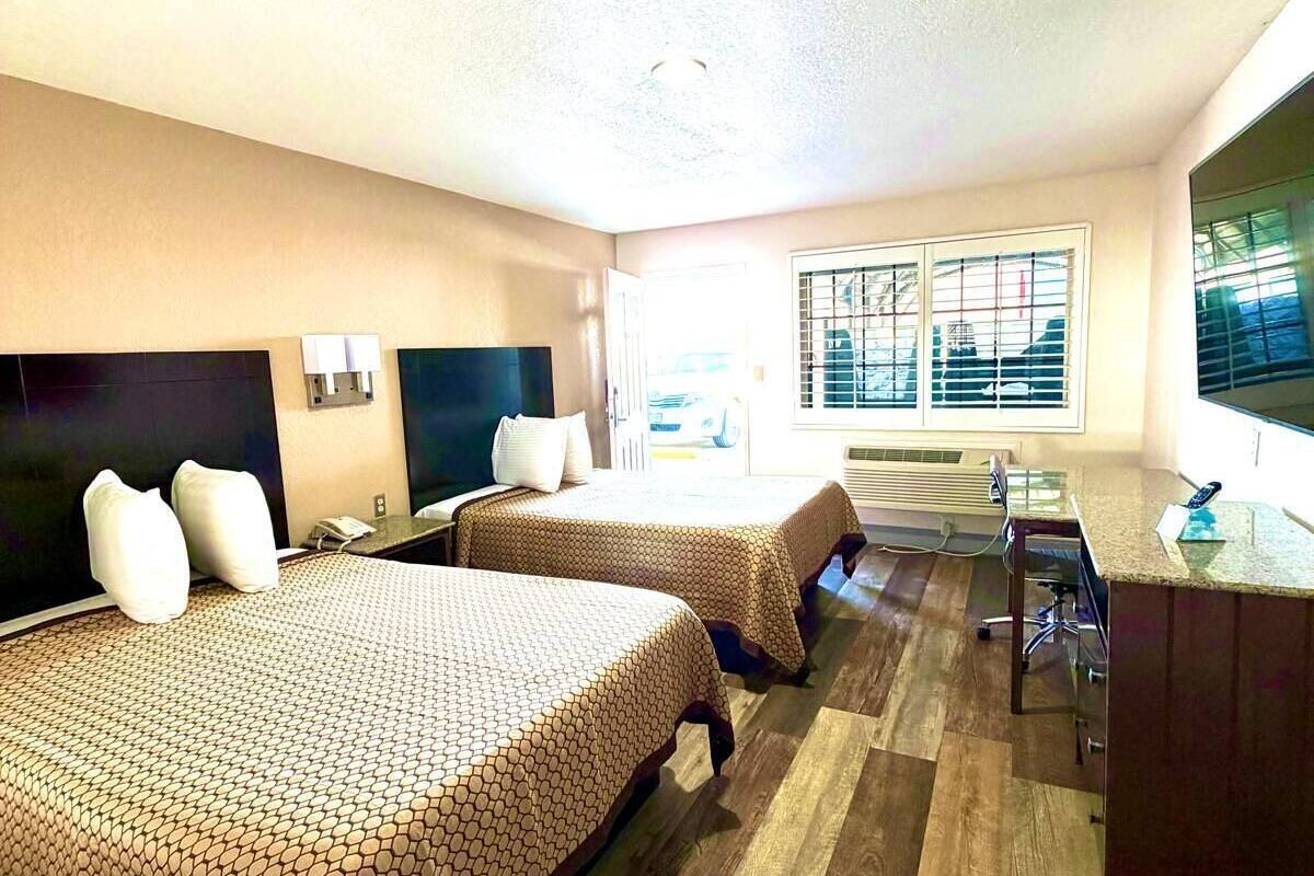 Een hotelkamer met twee bedden, een bureau en een groot raam met jaloezieën.