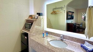 A bathroom with a granite countertop, a sink, a mirror, a towel rack, and a microwave. - Kermit Inn (Kermit)