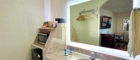 A bathroom with a granite countertop, a sink, a mirror, a towel rack, and a microwave.