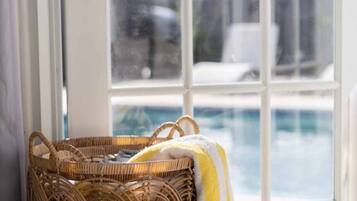 A wicker basket with a yellow and white striped towel beside a glass door leading to a pool area.