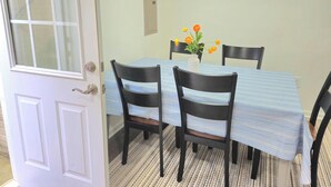 En matplats med ett bord täckt av en randig duk, fyra svarta stolar och en vas med orange blommor.