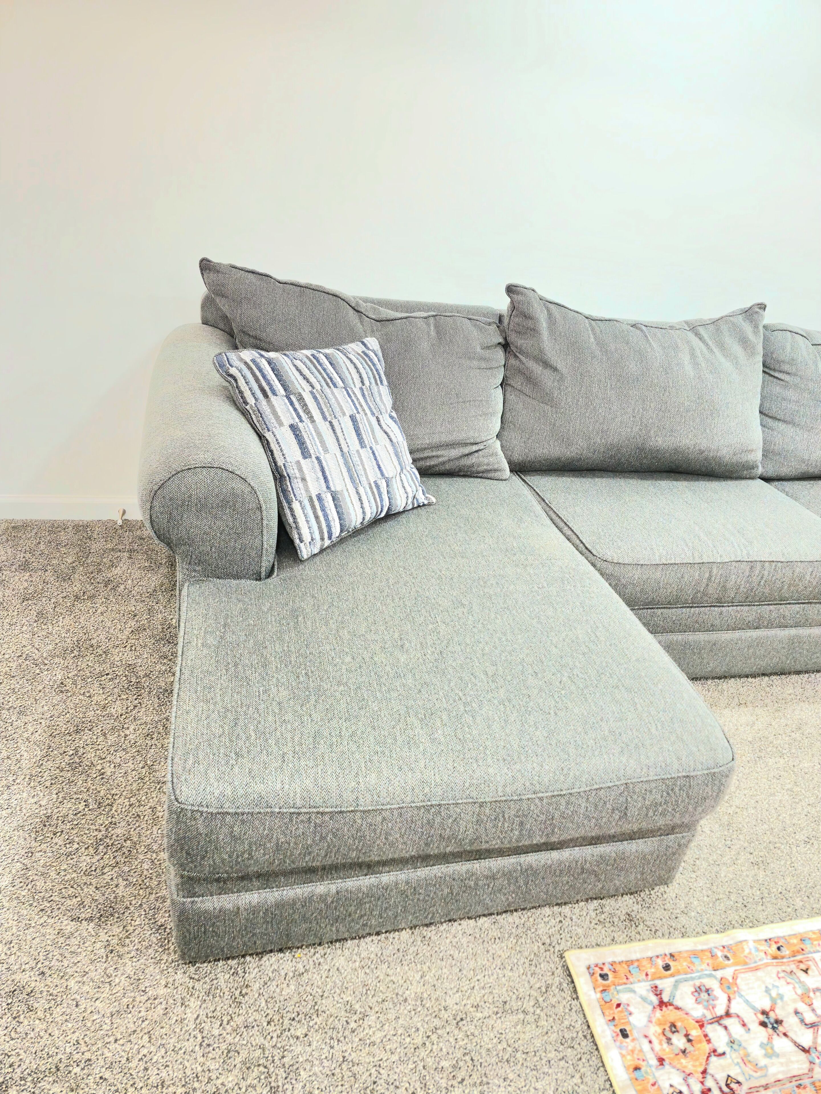 Un canapé d’angle gris avec un coussin à rayures et un tapis à motifs.