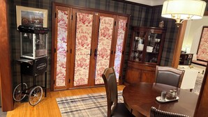 A dining area with a wooden table, chairs, a plaid rug, a popcorn machine, and a cabinet with glass doors. - Charming Furnished Tudor Revival in the Heart of Historic California Heights (Long Beach)