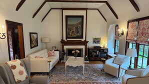 A cozy living room with a fireplace, a sofa, armchairs, and a coffee table. - Charming Furnished Tudor Revival in the Heart of Historic California Heights (Long Beach)
