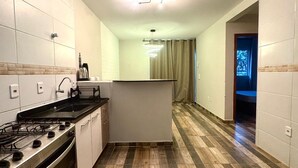 Eine schmale Küche mit Gasherd, Spüle und einer kleinen Kochinsel. Der Boden ist mit einem holzartigen Muster gefliest.