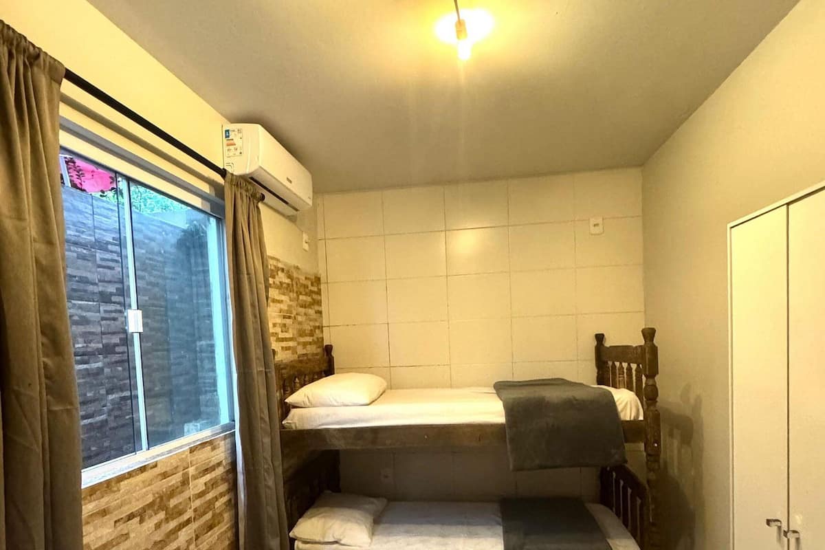 A dormitory room with bunk beds, a window with curtains, an air conditioning unit, and a wardrobe.
