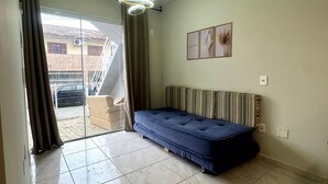 Ein Zimmer mit einem Bett, einer Deckenleuchte, einem Fenster mit Vorhängen und Blick auf ein Gebäude.