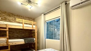 Ein Zimmer mit Etagenbetten, einem Einzelbett, einem Vorhangfenster, einer Klimaanlage und einer Deckenleuchte.
