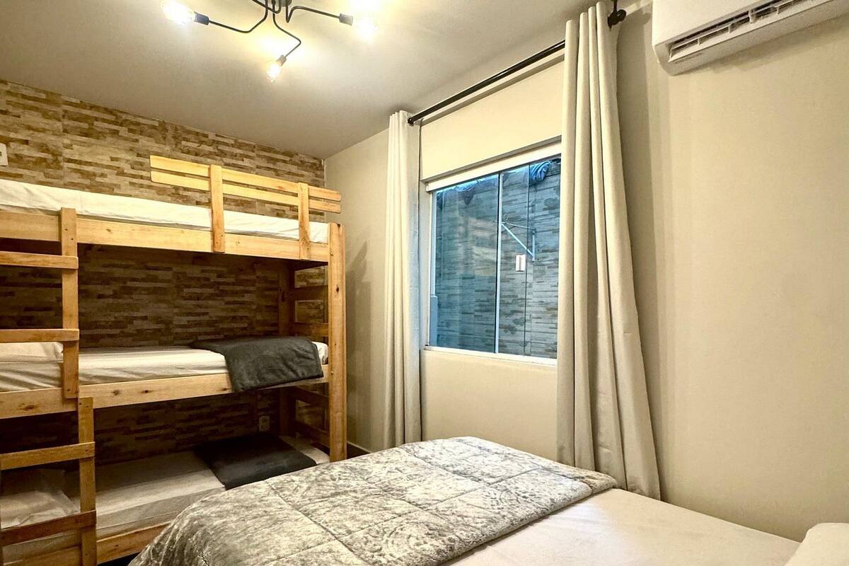 A room with bunk beds, a single bed, a window with curtains, an air conditioning unit, and a ceiling light fixture.