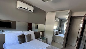 Une chambre d’hôtel avec un grand lit, un téléviseur à écran plat, un miroir et un appareil de climatisation.