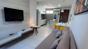 Un salon moderne doté d’un téléviseur à écran plat, d’un canapé, d’une table basse et d’un coin repas avec une table mise pour deux personnes.
