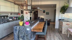 Une cuisine moderne dotée d’un îlot central, un coin repas avec une banquette et un espace de vie comprenant un canapé et un tableau.