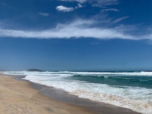 A beach with waves, a clear sky, and a distant landform. - Cobertura dos Jades c Jacuzzi - Campeche (Florianópolis)