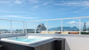 Une terrasse sur le toit avec un jacuzzi, de grandes fenêtres et une vue sur les montagnes et les bâtiments.