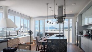 Une cuisine moderne dotée d’un grand îlot central, d’un coin repas offrant une vue agréable et d’une grande fenêtre donnant sur le paysage urbain.