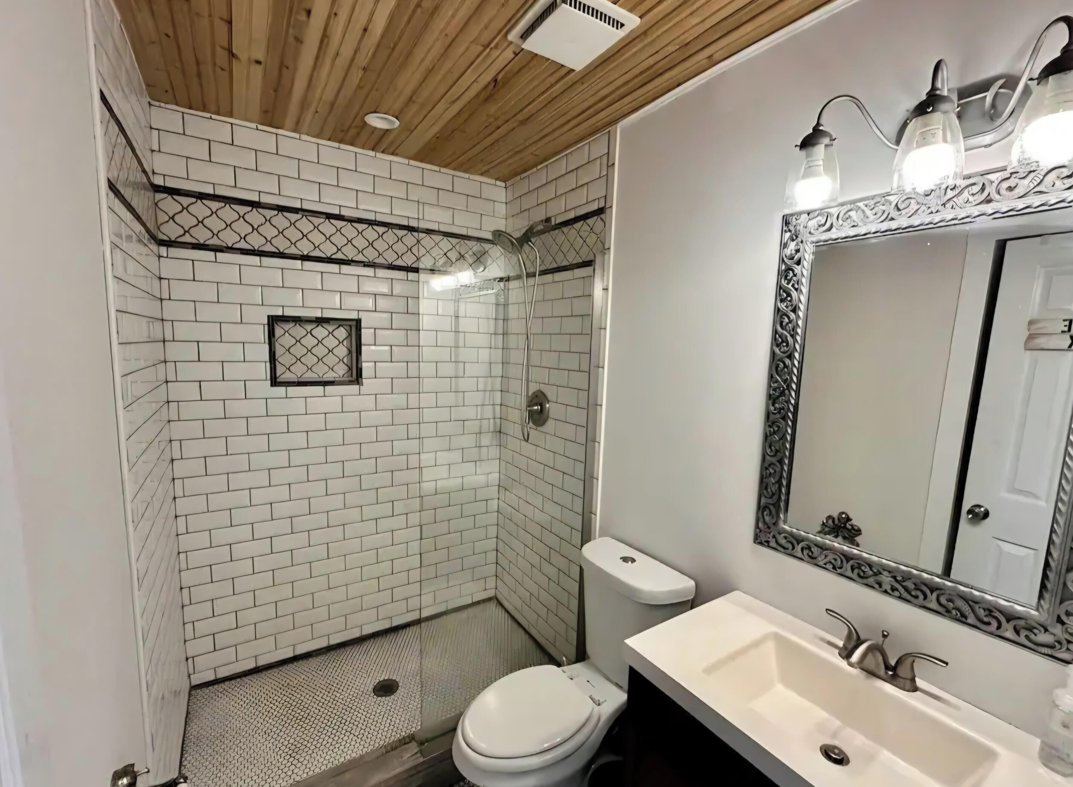 Een badkamer met witte metro tegels, een douche, toilet, wastafel en een spiegel met een sierlijk lijstwerk.