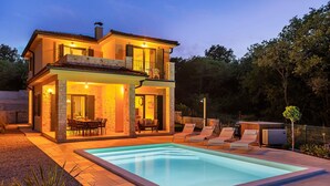 Ein zweistöckiges Haus mit Swimmingpool, Sitzgelegenheiten im Freien und einer gut beleuchteten Terrasse.