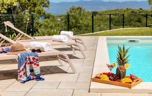 A poolside area with lounge chairs, towels, and a tray of fruit and drinks. - Amazing home in Vrbnik with sauna (Vrbnik)