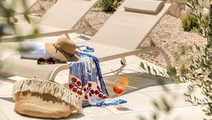 Eine Liege mit Hut, Sonnenbrille, Handtuch und einem Getränk mit Orangenscheibe.