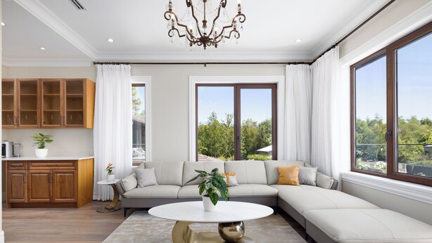 Un salon moderne avec un canapé d’angle, une table basse ronde et une grande fenêtre donnant sur un paysage verdoyant.