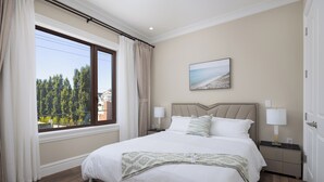 Une chambre avec un grand lit, une fenêtre avec des rideaux, une table de chevet avec une lampe et un tableau au mur.