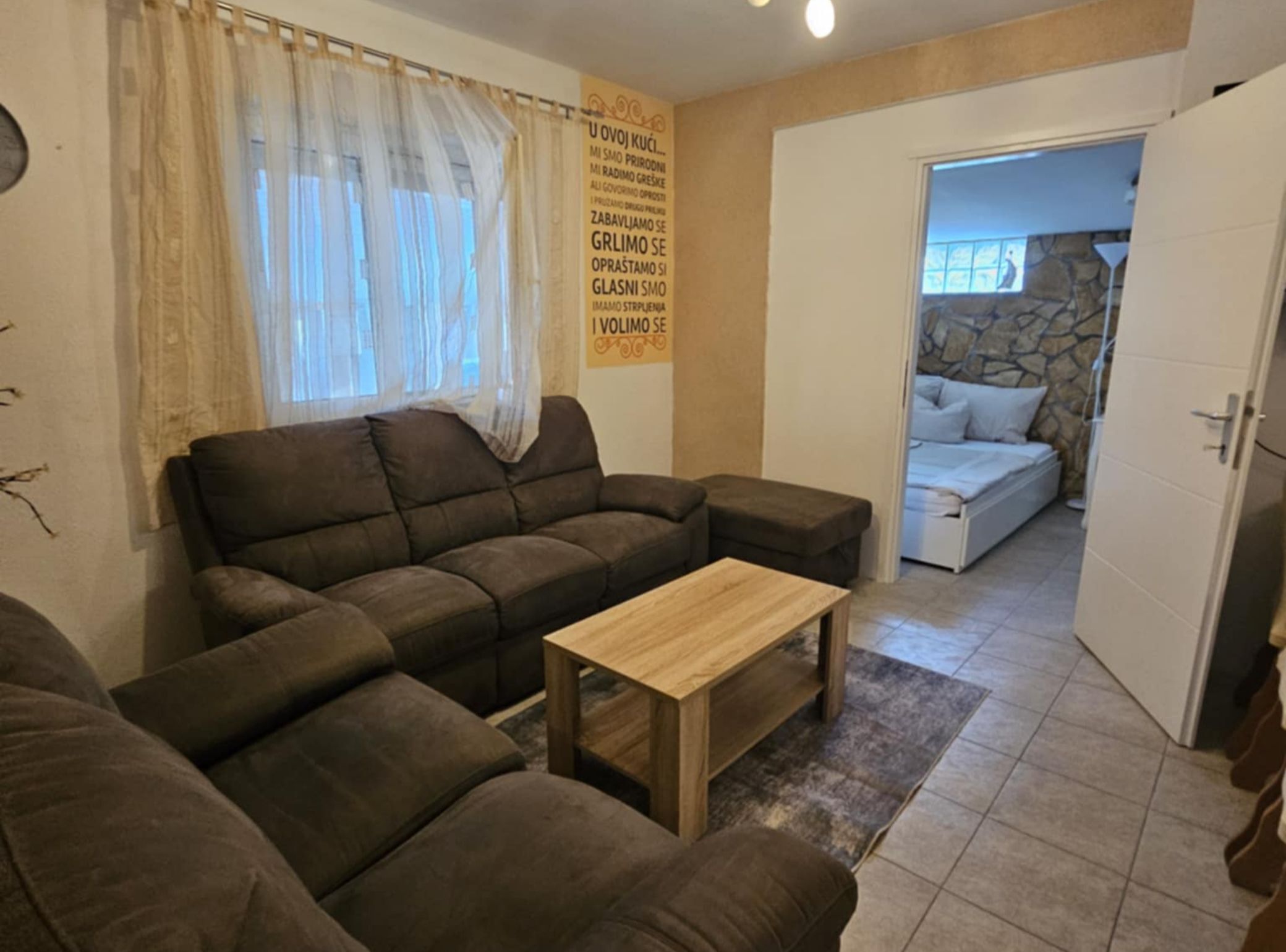 Uma sala de estar com um sofá marrom, uma mesa de centro de madeira e uma parede de pedra ao fundo.