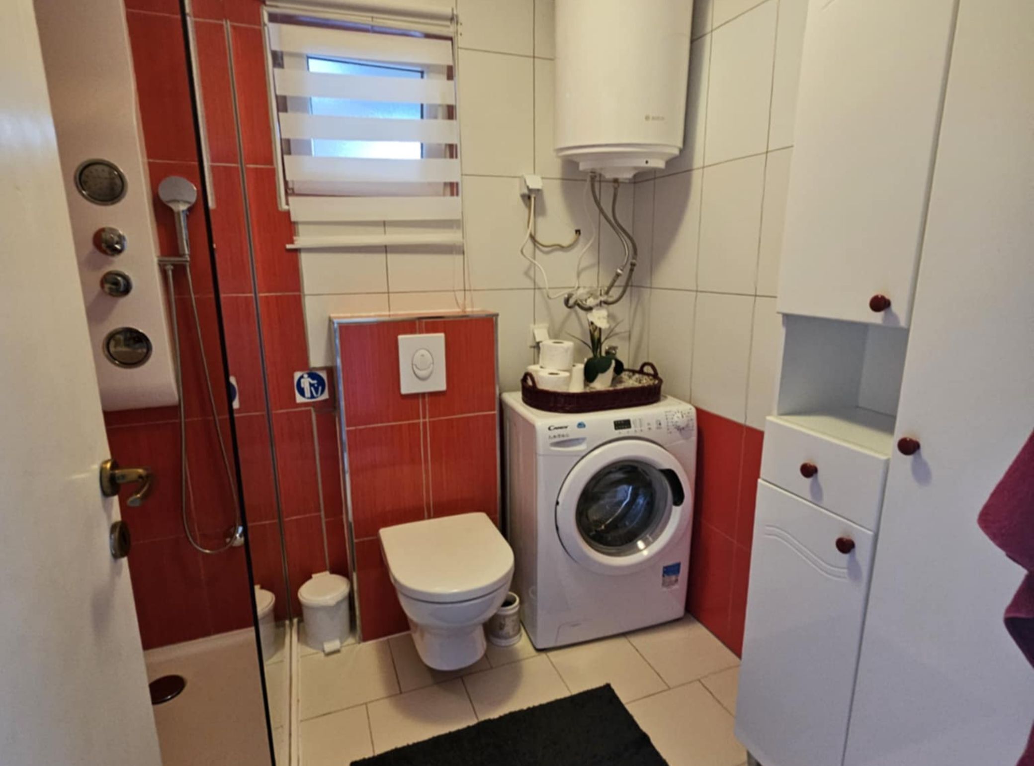 Een kleine badkamer met toilet, wasmachine en douche.