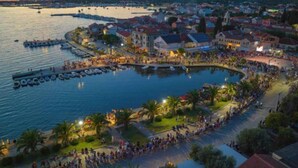 Uma vila costeira com um porto de iates, calçadão à beira-mar e edifícios residenciais.