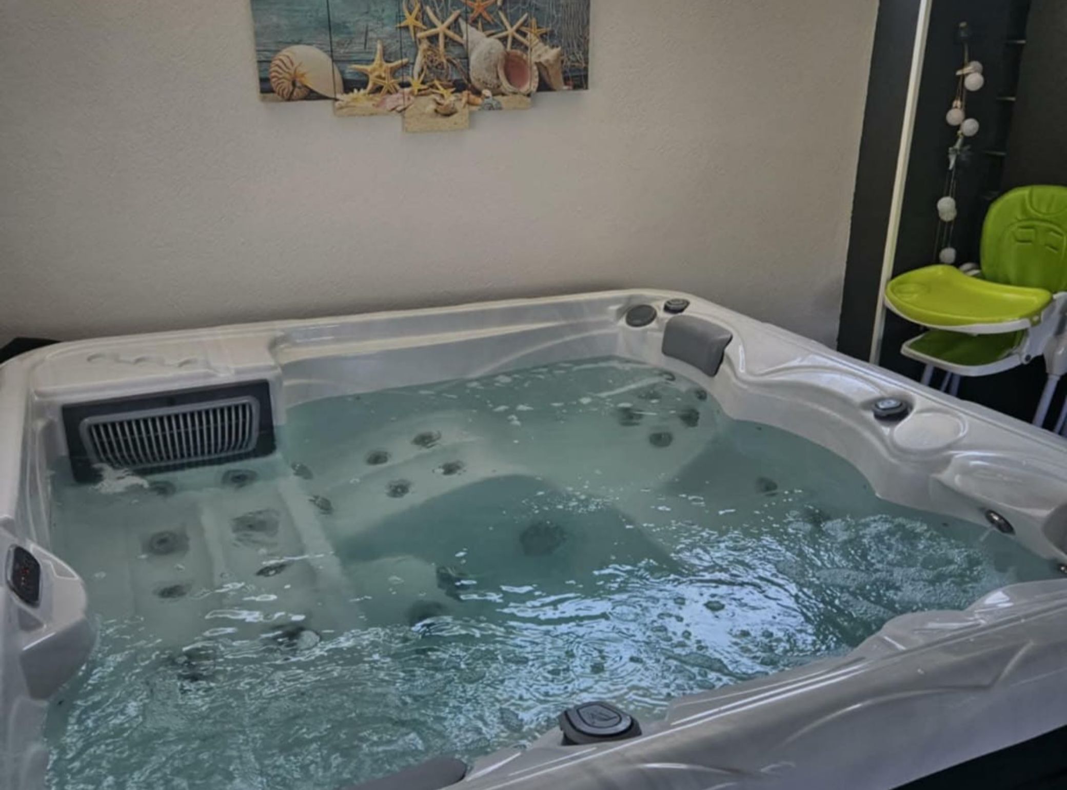 Un bain à remous équipé d’une bouche d’aération, de jets à bulles, et avec une chaise verte à proximité.