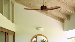 Ein Zimmer mit Holzboden, Deckenventilator, Bett mit gestreifter Bettwäsche, rundem Spiegel und Topfpflanze.