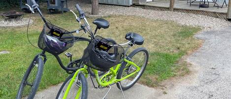 Una bicicleta estacionada sobre un sendero de hormigón, con un cobertizo metálico y mobiliario exterior al fondo.