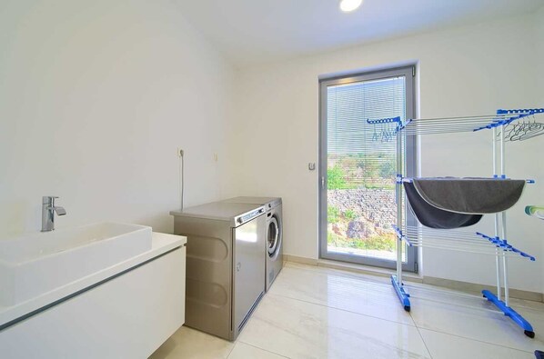 A modern bathroom with a built-in washing machine, a sink, and a drying rack. - Villa SIA with private pool (Krk)