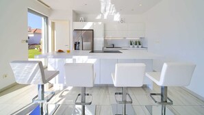A modern kitchen with white cabinetry, a stainless steel refrigerator, and a central island with bar stools.