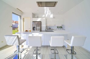 A modern kitchen with white cabinetry, a stainless steel refrigerator, and a central island with bar stools. - Villa SIA with private pool (Krk)