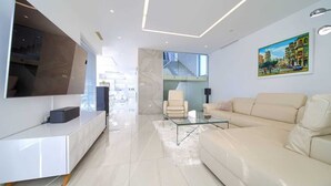 A modern living room with a white sofa, a glass coffee table, and a large flat-screen TV mounted on the wall.