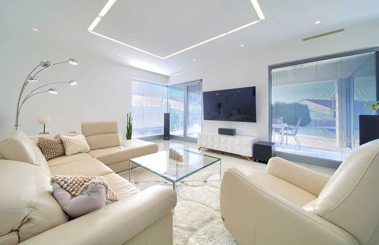 Ein modernes Wohnzimmer mit einer Couch, Sesseln, einem Glastisch und einem an der Wand befestigten Flachbildfernseher.