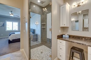 Un baño moderno con cabina de ducha de vidrio, tocador de mármol y un espejo grande.
