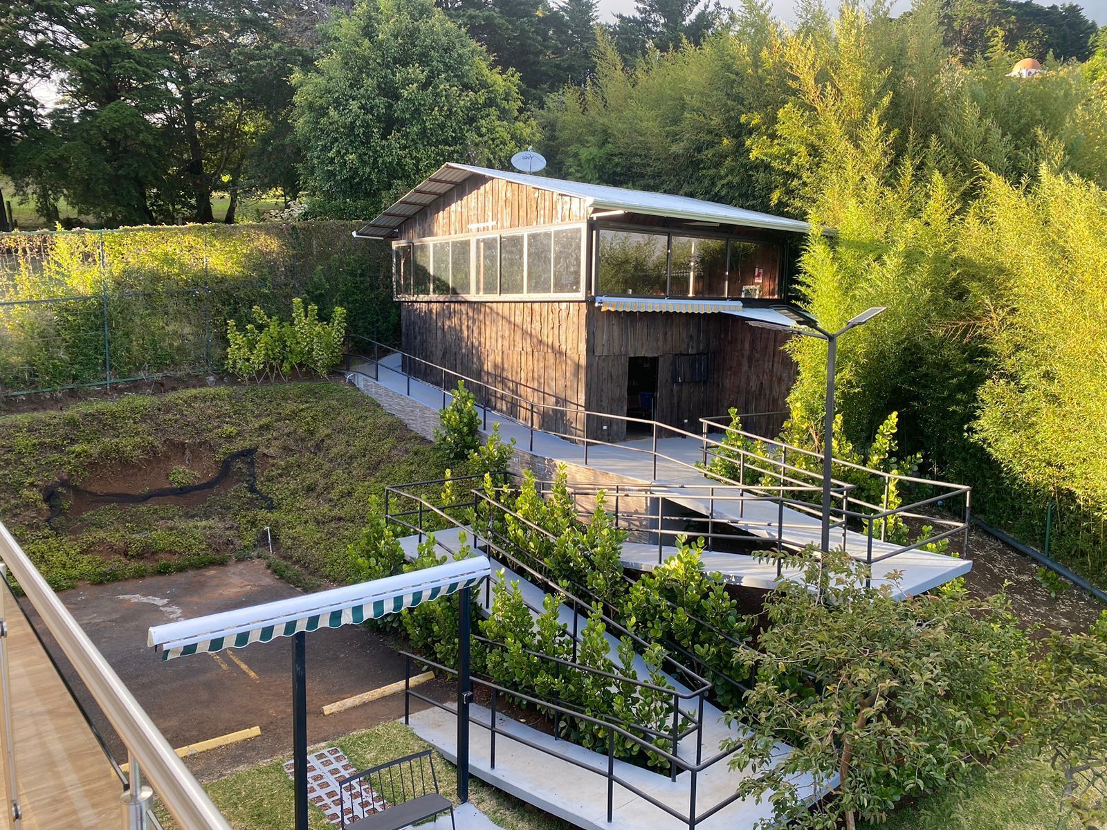 Uma cabana moderna de madeira com extensão de vidro, rodeada por vegetação exuberante e paisagem inclinada.