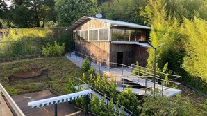A modern wooden cabin with a glass extension, surrounded by lush greenery and a sloped landscape. - Luxurious Suits 9 Bedrooms Building (Heredia)