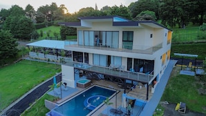 Una casa moderna de dos pisos con una amplia piscina, mobiliario de exterior y un césped bien cuidado.