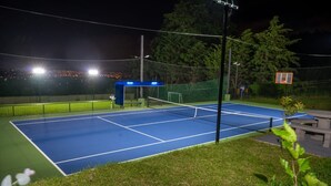 An outdoor tennis court at night with a blue surface, surrounded by a green fence, and a small shelter with a blue roof. - Luxurious Suits 9 Bedrooms Building (Heredia)