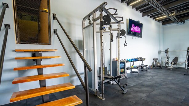 A gym with wooden steps, weightlifting equipment, and a neon sign. - Luxurious Suits 9 Bedrooms Building (Heredia)