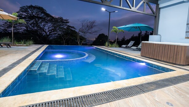 Una piscina con borde de azulejos, terraza de madera y sillas de descanso.