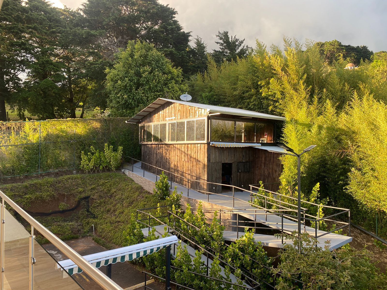 Uma cabana moderna de madeira com extensão de vidro, rodeada por vegetação exuberante e um deck de madeira.