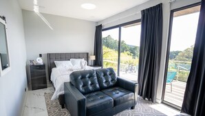 A modern hotel room with a large bed, a black leather sofa, and a balcony with a view of greenery. - Luxurious Suits 9 Bedrooms Building (Heredia)