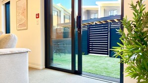 Ein modernes Zimmer mit einer Schiebetür zu einem Garten und einer grauen Couch, sowie einem Topf mit einer Pflanze.
