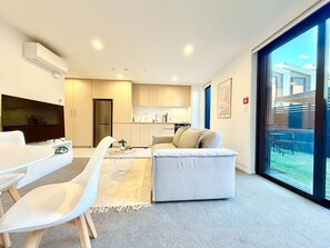 Una sala de estar moderna con sofá, una mesa de comedor con sillas, una zona de cocina y un amplio ventanal con vistas al exterior.